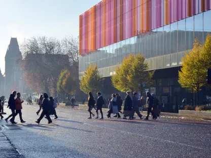 People crossing a busy Oxford Road in front of the Alliance Manchester Business School building