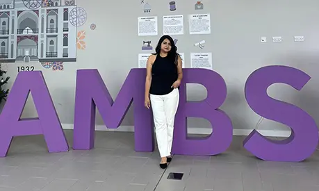 Niharika Singh, a student at Alliance Manchester Business School, standing in front of large purple letters on campus.