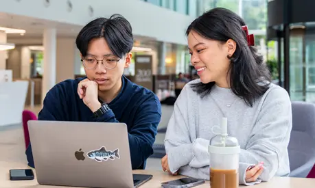 Two students sitting in front of a laptop on a table in the AMBS reception