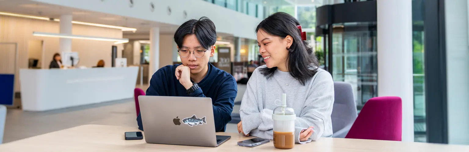 Two students sitting in front of a laptop in the AMBS reception