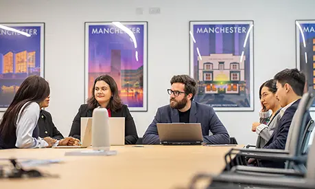 Six MBA students working on laptops in a boardroom.