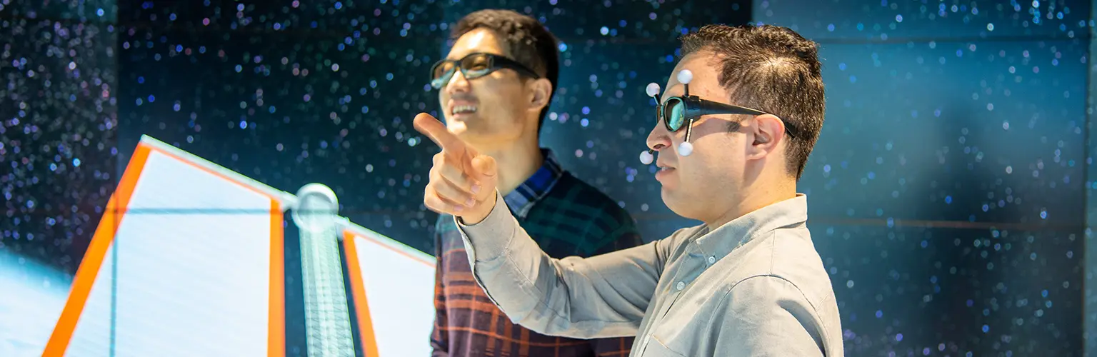 Two people stood in a data visualisation observatory wearing 3D glasses and pointing at the images in front of them