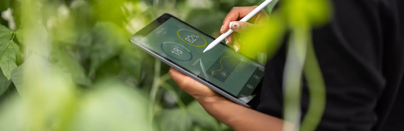 person holding a tablet showing statistics in front of plants