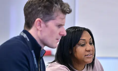 Two professionals sat at a table looking at a laptop together