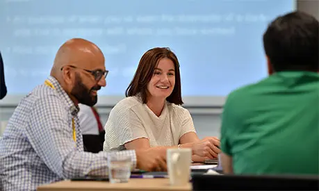 A male and a female dressed in professional clothing talking to other class mates across the table who are out of the frame