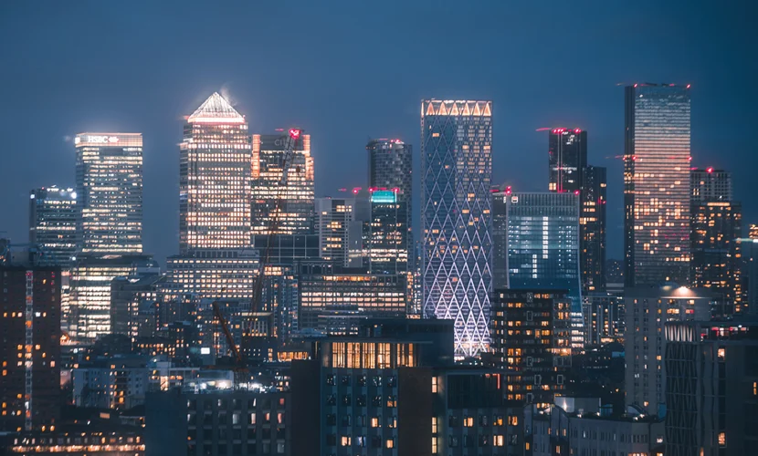 An aerial view of multiple tall buildings in the Canary Wharf skyline at night