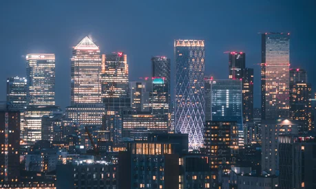 An aerial view of multiple tall buildings in the Canary Wharf skyline at night