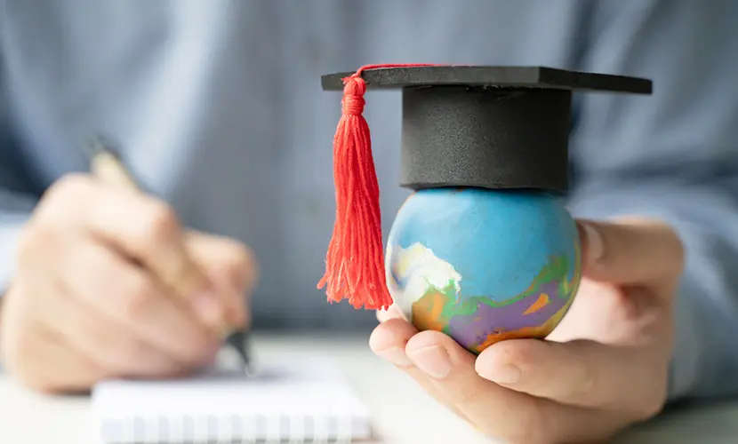 Image of a person holding a small world globe with a graduate hat placed on top.