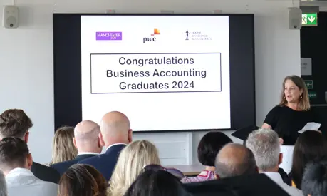 A room full of graduates looking at a presentation screen that reads 'Congratulations Business Accounting Graduates 2024'