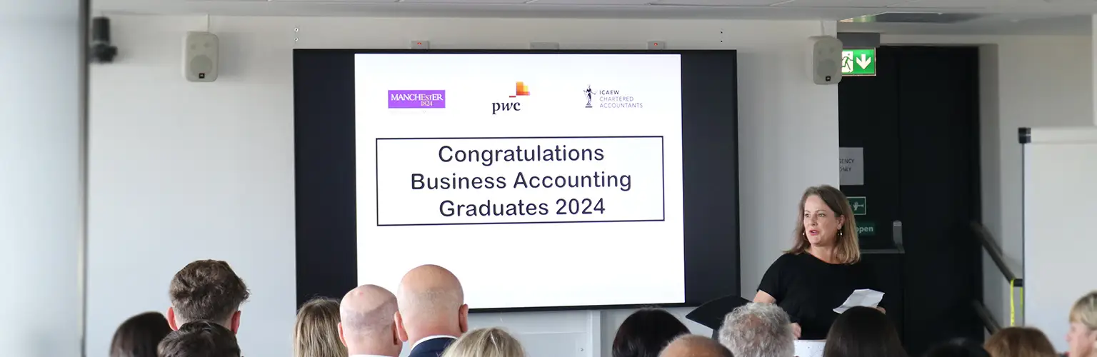 A room full of graduates looking at a presentation screen that reads 'Congratulations Business Accounting Graduates 2024'