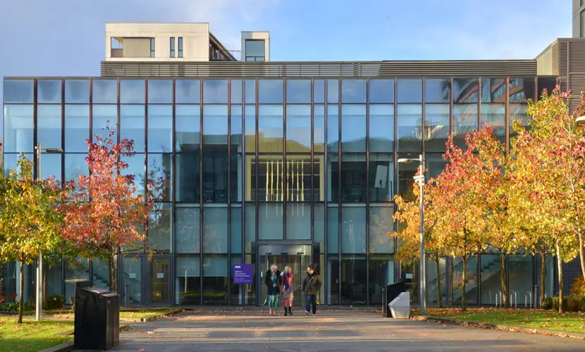 Three AMBS colleagues walking outside the AMBS executive education building with autumnal trees surrounding them