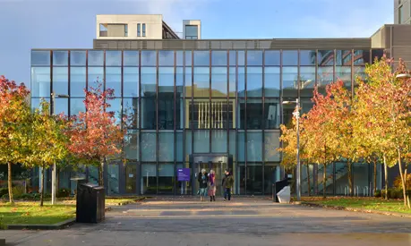 Three AMBS colleagues walking outside the AMBS executive education building with autumnal trees surrounding them