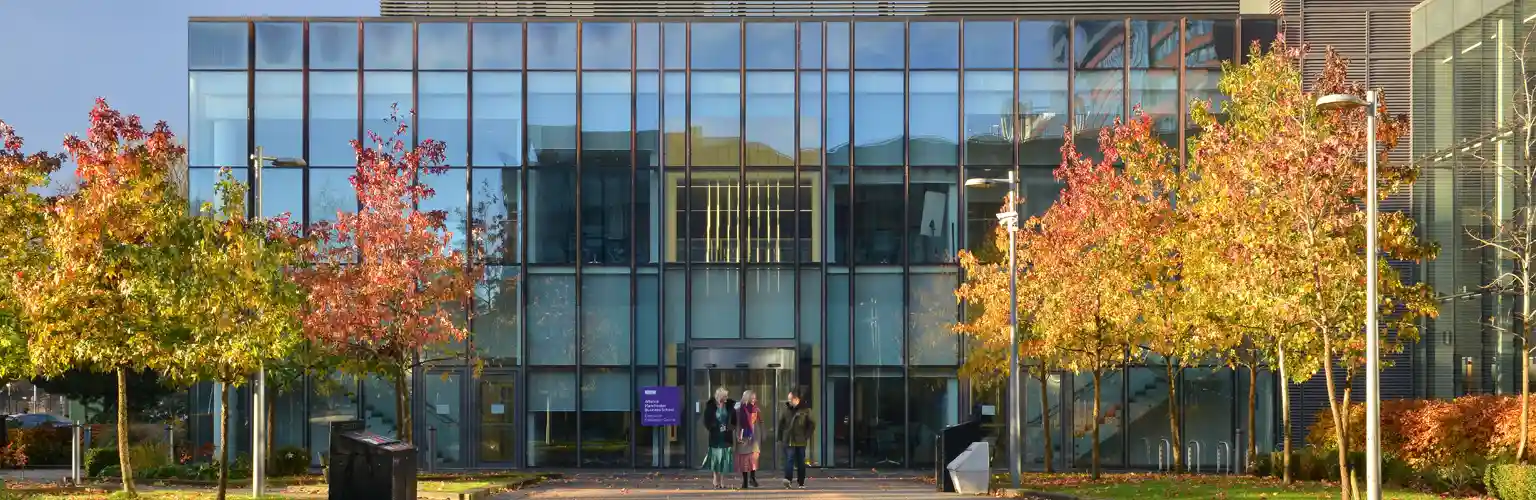 Three AMBS colleagues walking outside the AMBS executive education building with autumnal trees surrounding them