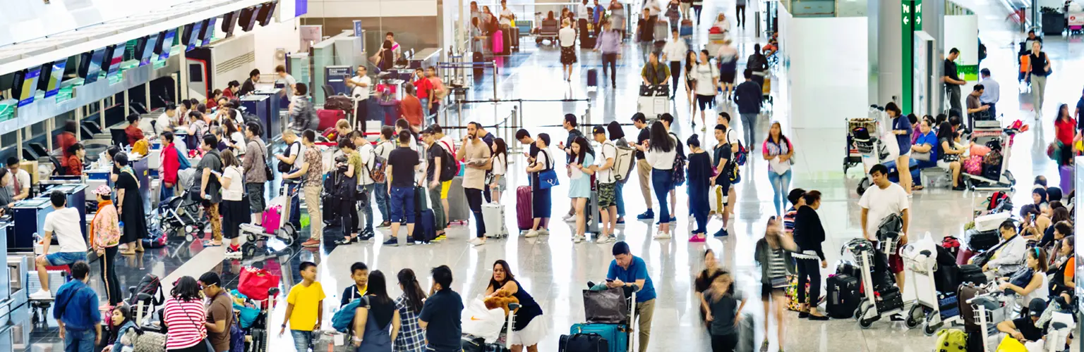 A large crowd of people waiting at a check-in desk in a busy airport