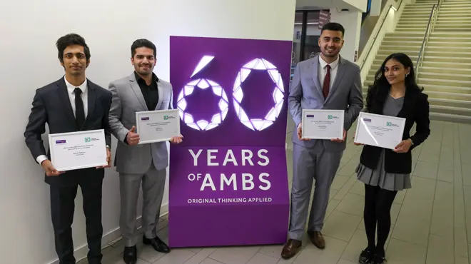 Members of the team 'Case Closed', winners of the MBA Case Interview Competition, in front of a light-up box that reads '60 years of AMBS'