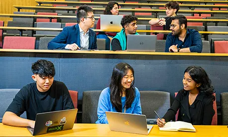 Eight master's students working on laptops and talking in a lecture theatre.