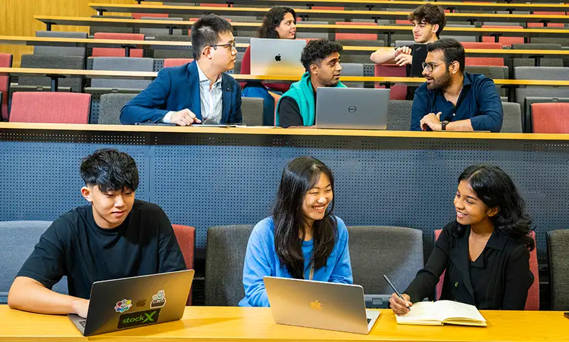 Eight master's students working on laptops and talking in a lecture theatre.