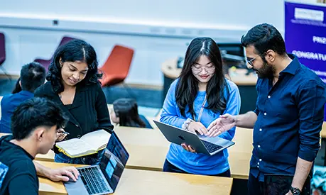 Four students working together on laptops in a lecture theatre.