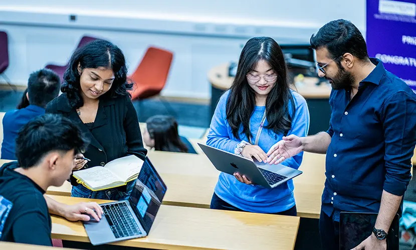 Four students working together on laptops in a lecture theatre.