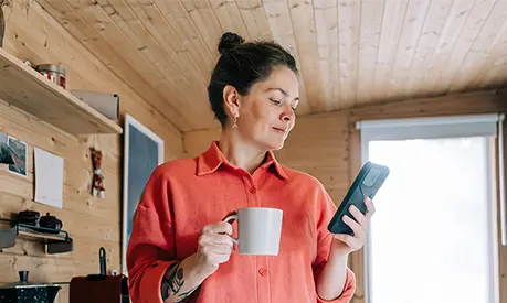 Woman enjoying morning coffee and checking her phone in rustic kitchen.