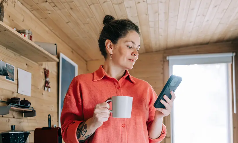 Woman enjoying morning coffee and checking her phone in rustic kitchen.