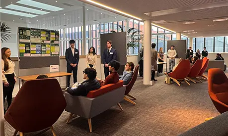 ITMB and MSc Digital Transformation students presenting project posters to employers at the AMBS ITMB Showcase, with small audiences seated in a modern open space.