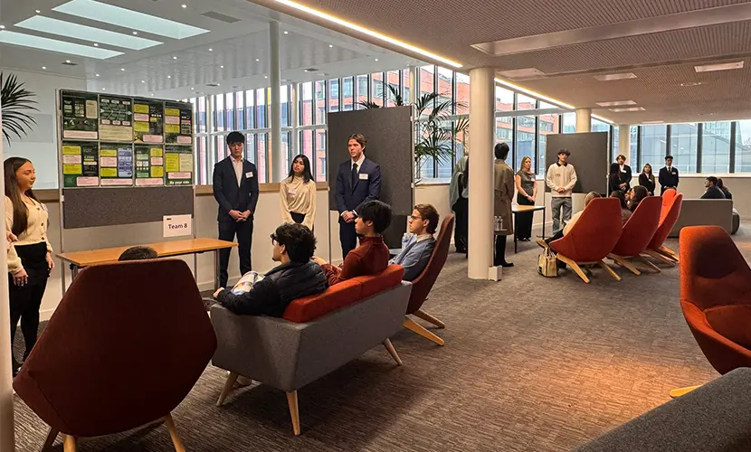ITMB and MSc Digital Transformation students presenting project posters to employers at the AMBS ITMB Showcase, with small audiences seated in a modern open space.
