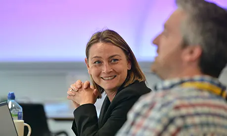 Woman in classroom environment dressed in professional clothing smiling at the person next to them