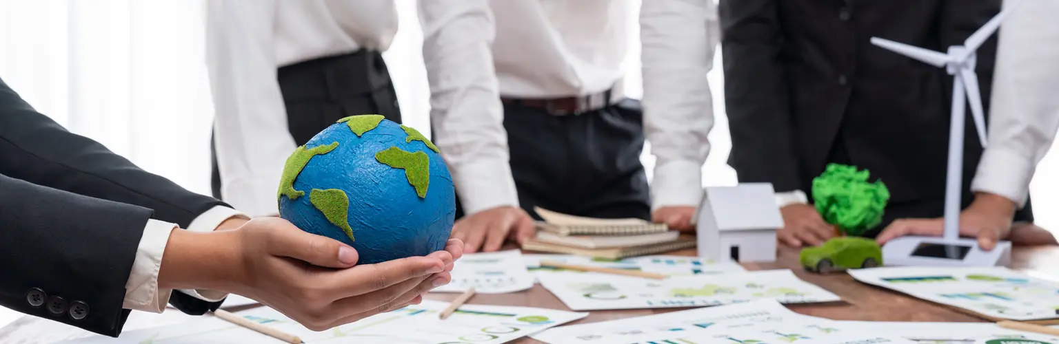 Businessman hand holding paper Earth with business people on meeting in office, planning and implementing eco-friendly ideal for corporate policy to reduce CO2 emission and save earth.