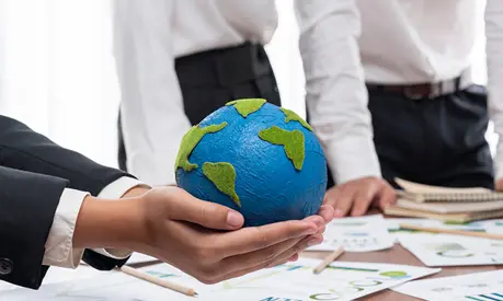 Businessman hand holding paper Earth with business people on meeting in office, planning and implementing eco-friendly ideal for corporate policy to reduce CO2 emission and save earth.