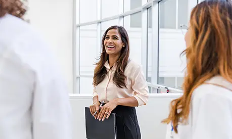 A woman holding a folder smiles while talking with her colleagues.