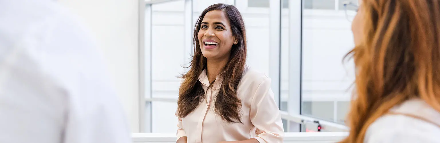 A woman holding a folder smiles while talking with her colleagues.