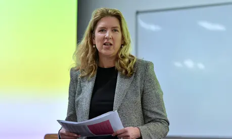 A woman lecturer stands at the front of a classroom holding papers