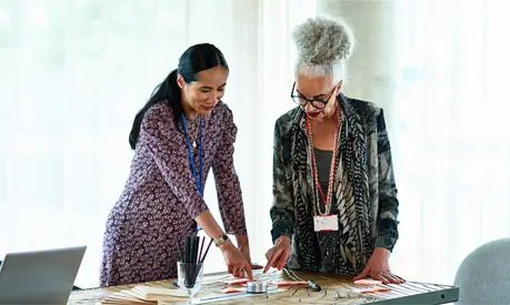 Two professional women in an office comparing different post-it notes on a table