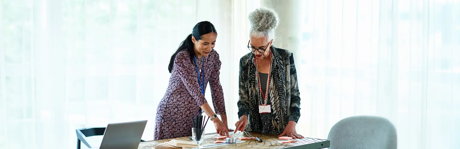 Two professional women in an office comparing different post-it notes on a table