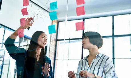 Two female professionals working together and writing notes on a whiteboard